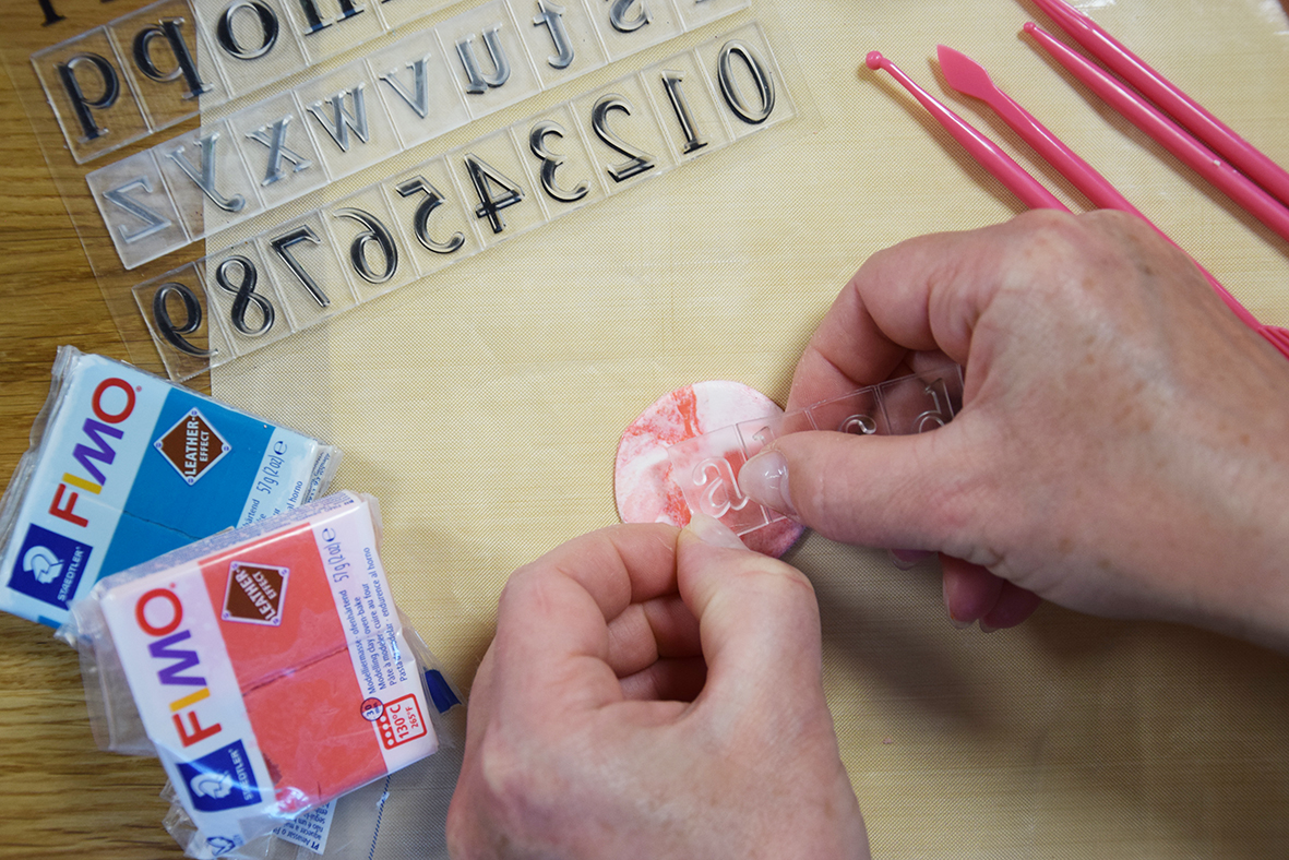 Žena pomocou silikónových pečiatok v tvare malej abecedy vytláča do stredu vykrojených krúžkov písmená.